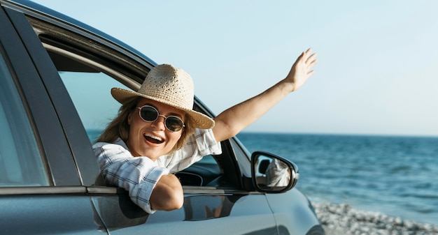 Feliz mujer rubia con sombrero mirando por la ventanilla del coche