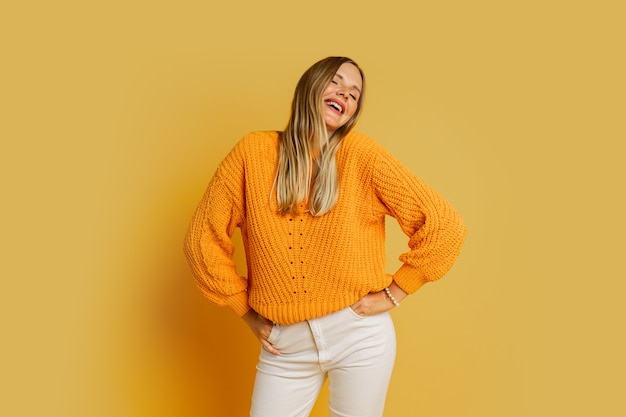 Foto gratuita feliz mujer rubia en suéter de otoño con estilo naranja posando en amarillo.