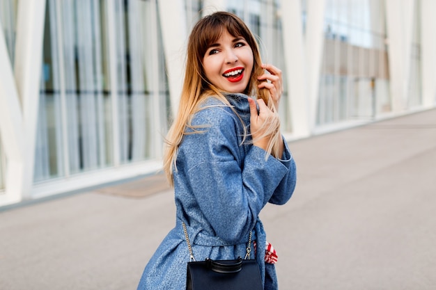 Feliz mujer segura caminando por la calle moderna en elegante abrigo de lana azul