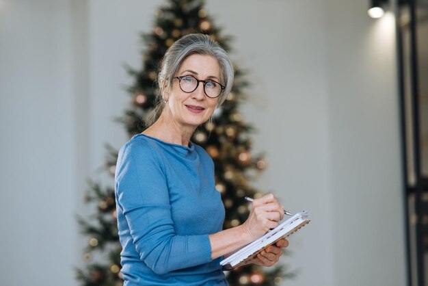 Feliz mujer senior en gafas escribiendo en un cuaderno en casa