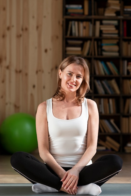 Foto gratuita feliz mujer sentada en la estera de yoga posando