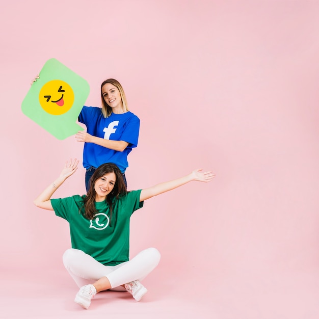 Feliz mujer sentada frente a su amiga con un guiño de emoji guiñando un ojo