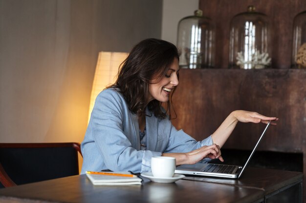 Feliz mujer sentada en el interior usando la computadora portátil