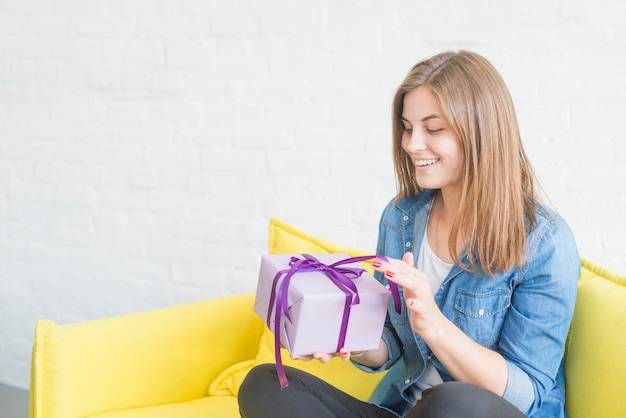 Feliz mujer sentada en el sofá abriendo regalo de San Valentín