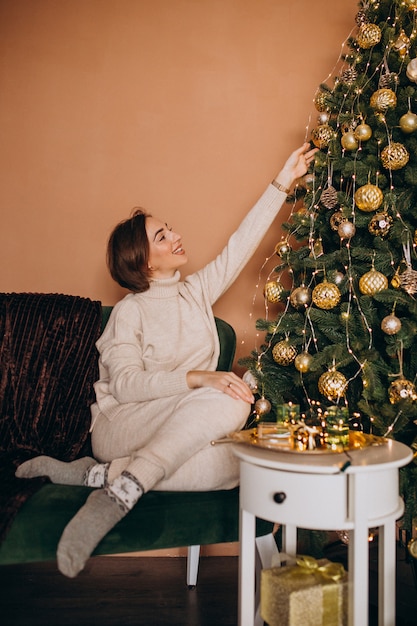 Feliz mujer sentada en el sofá junto al árbol de navidad