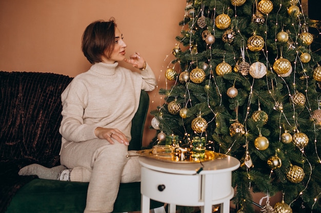 Feliz mujer sentada en el sofá junto al árbol de Navidad