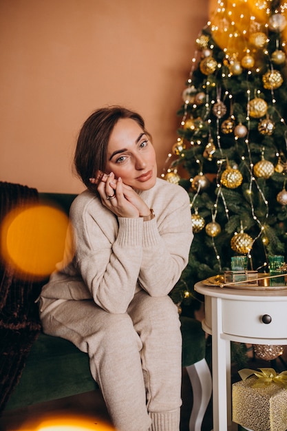 Feliz mujer sentada en el sofá junto al árbol de navidad