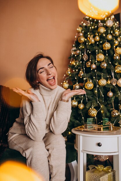 Feliz mujer sentada en el sofá junto al árbol de Navidad