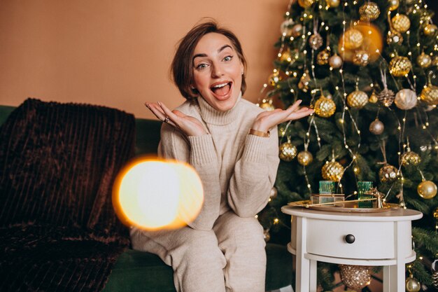Feliz mujer sentada en el sofá junto al árbol de Navidad