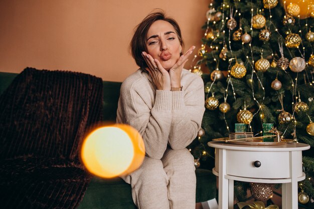 Feliz mujer sentada en el sofá junto al árbol de Navidad