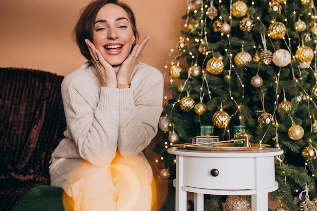 Feliz mujer sentada en el sofá junto al árbol de Navidad