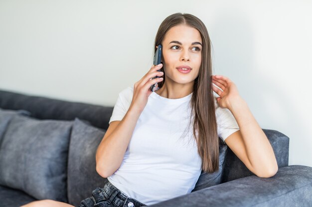 Feliz mujer sentada en su sofá en el teléfono en su casa en la sala de estar