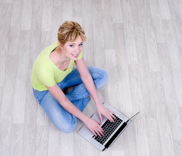 Feliz mujer sentada en el suelo con ordenador portátil - vista de ángulo alto