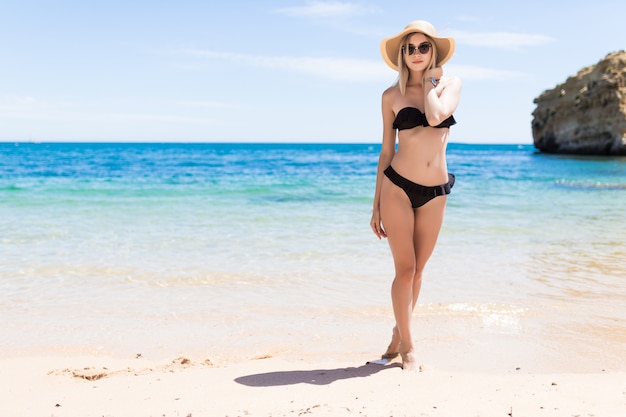 Feliz mujer sonriente en bikini y sombrero para el sol en la playa del mar