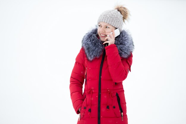 Feliz mujer sonriente en la chaqueta de invierno rojo habla por teléfono móvil, al aire libre, contra la nieve