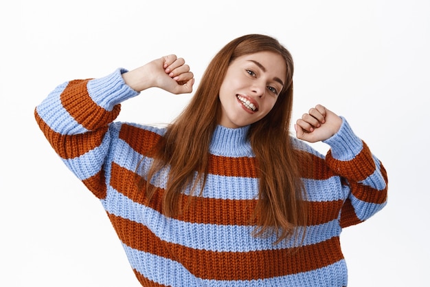 Foto gratuita feliz mujer sonriente estirando las manos hacia arriba, bailando y divirtiéndose en el ocio, relajándose y mirando despreocupado, pared blanca