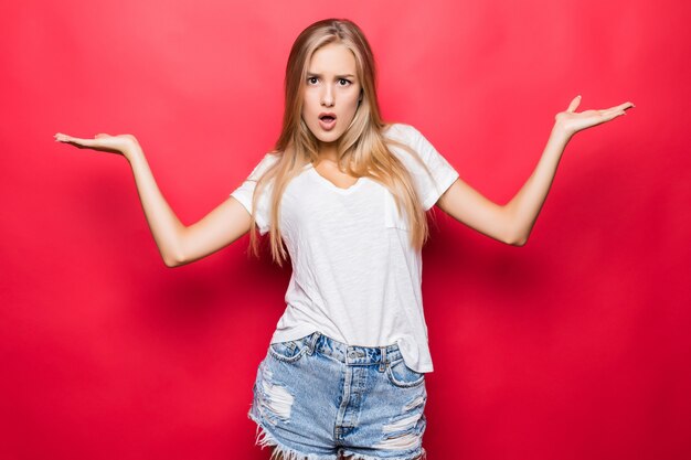 Feliz mujer sonriente gesticulando con las manos y mostrando equilibrio aislado sobre fondo rojo.