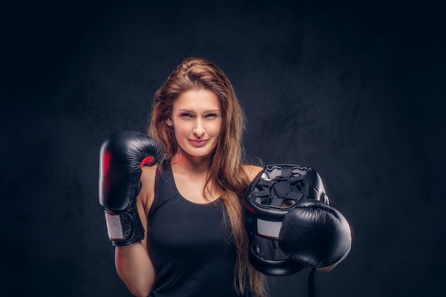 Feliz mujer sonriente con guantes de boxeador sostiene casco protector en el estudio.