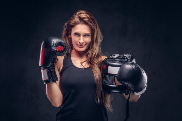 Feliz mujer sonriente con guantes de boxeador sostiene casco protector en el estudio.