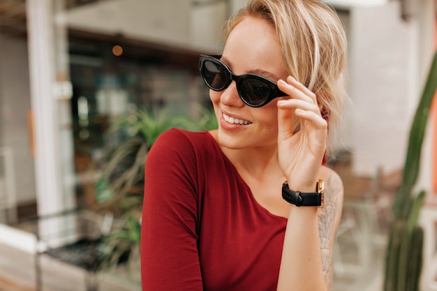 Feliz mujer sonriente sosteniendo gafas de sol y mirando con sonrisa