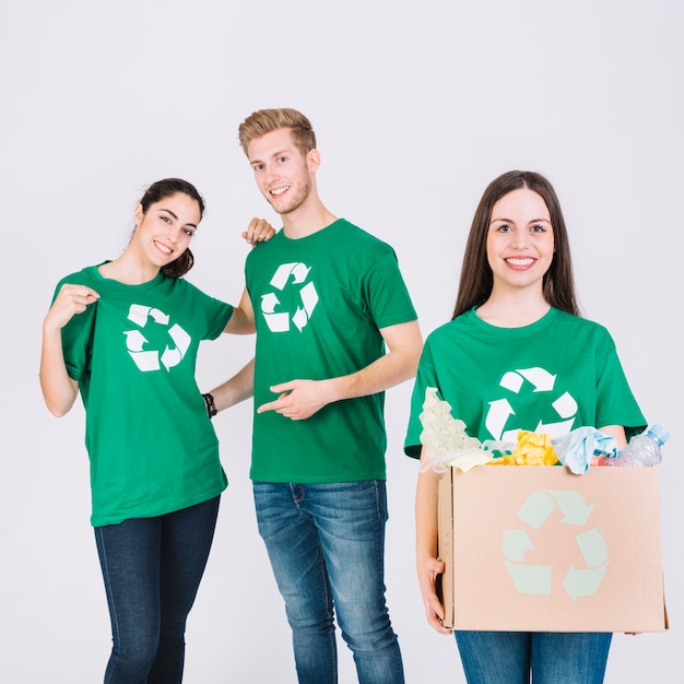 Foto gratuita feliz mujer sosteniendo la caja de cartón con artículos de reciclaje en frente de sus amigos