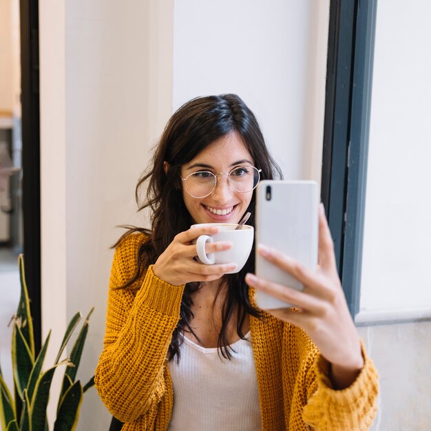 Feliz mujer con taza de conseguir selfie sonriendo