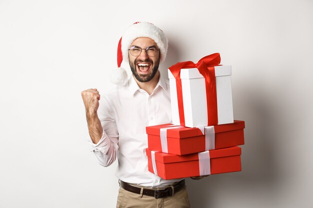 Feliz navidad, concepto de vacaciones. Hombre emocionado recibiendo regalos de Navidad y regocijo, vistiendo gorro de Papá Noel, celebrando el Año Nuevo