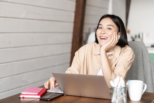 Feliz niña asiática escuchando seminarios web en línea asistir a clases de cursos de internet en la computadora portátil con tecnología inalámbrica ...