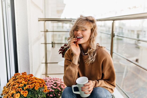 Feliz niña blanca disfrutando de un té en el balcón. Magnífica mujer joven relajándose en la terraza.
