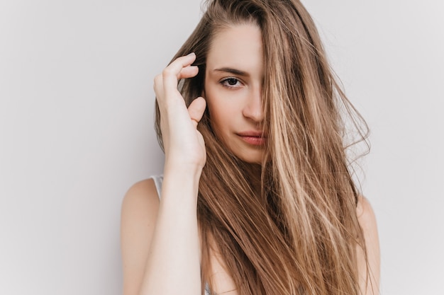 Feliz niña de ojos oscuros posando en la mañana. foto de encantadora modelo de mujer caucásica tocando su cabello oscuro.