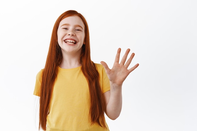 Feliz niña pelirroja niño niña muestra el número de cinco dedos y riendo sonriendo ampliamente de pie sobre fondo blanco.