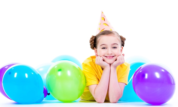 Feliz niña sonriente en camiseta amarilla tirada en el suelo con globos de colores - aislado en un blanco