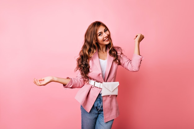 Feliz niña sonriente expresando buenas emociones en pastel. Modelo femenino atractivo en jeans y chaqueta rosa riendo.