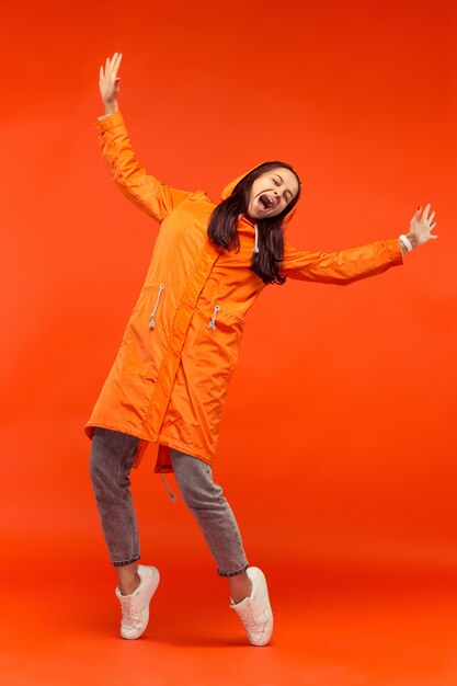 La feliz niña sonriente posando en el estudio en otoño chaqueta naranja aislada en la pared naranja