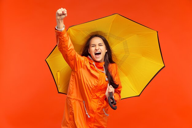 feliz niña sonriente posando en el estudio en otoño chaqueta naranja aislada en rojo. Emociones humanas positivas. Concepto de clima frío. Conceptos de moda femenina