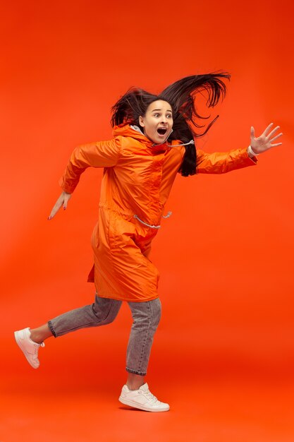 La feliz niña sonriente posando en el estudio en otoño chaqueta naranja aislada en rojo.