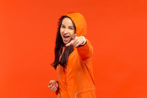 La feliz niña sonriente posando en el estudio en otoño chaqueta naranja apuntando a la cámara aislada en rojo