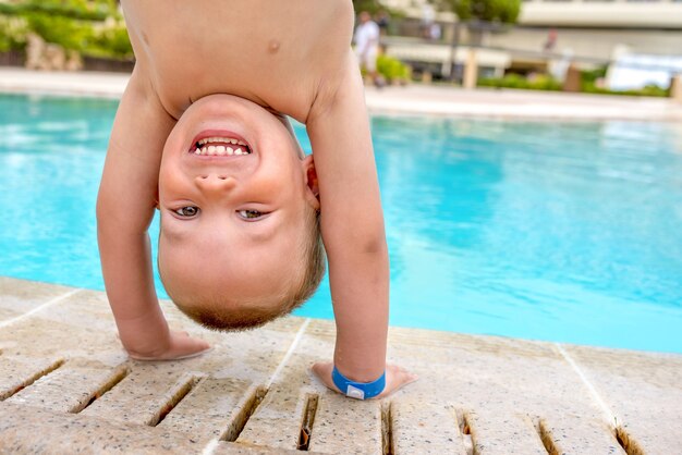 Feliz niño caucásico de pie en las manos cerca de la piscina