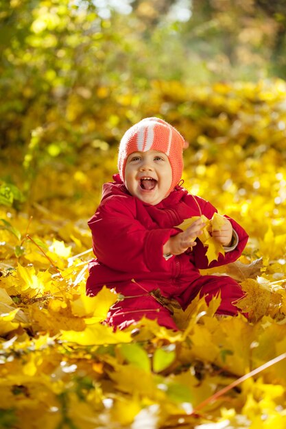 Feliz niño sentado en hojas de arce