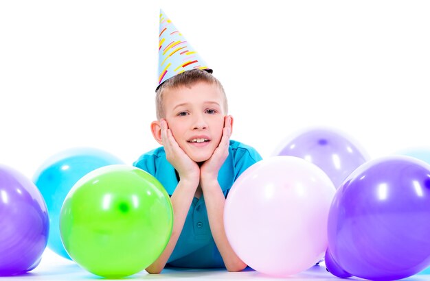 Feliz niño sonriente en camiseta azul tirado en el suelo con globos de colores y mostrando los pulgares hacia arriba - aislado en blanco