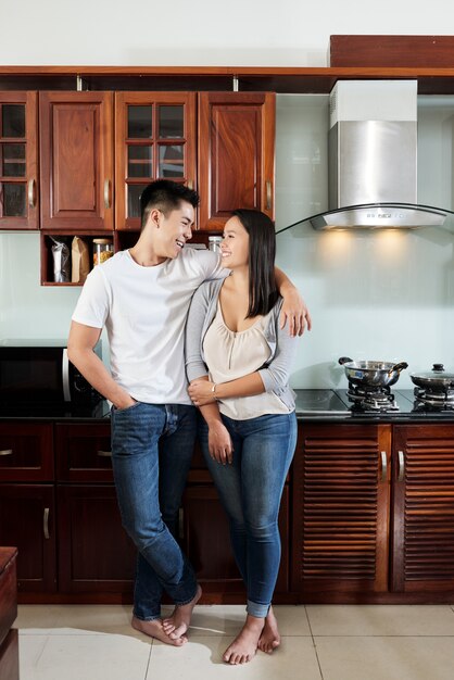 Feliz novio y novia asiáticos abrazándose y mirándose en la cocina