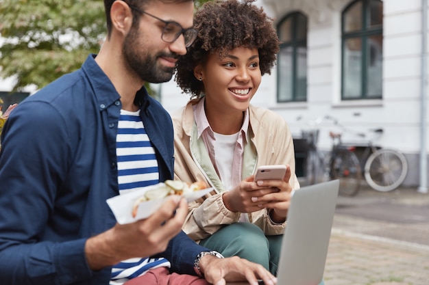 Feliz novio y novia de diferentes razas utilizan dispositivos modernos para la comunicación en línea