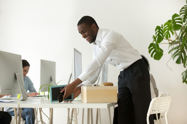 Feliz nuevo empleado africano desempaquetando pertenencias en el primer día laborable