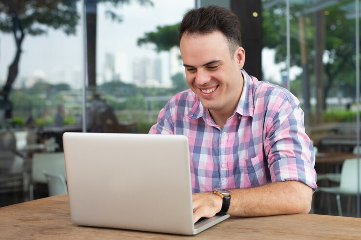 Foto gratuito feliz y optimista freelance trabajando con una computadora portátil en un café al aire libre