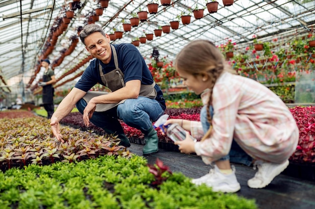 Feliz padre e hija alimentando flores en macetas mientras trabajan juntos en el vivero de plantas