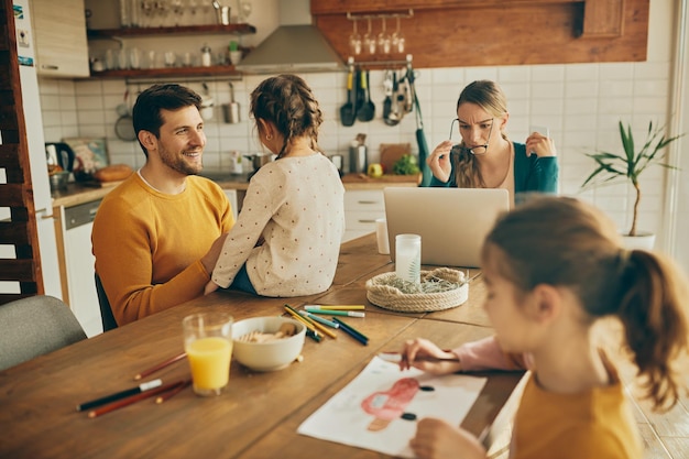 Feliz padre e hija hablando mientras la madre trabaja en una laptop en casa