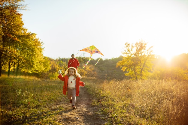 Feliz padre e hija linda caminando por el sendero del bosque en un día soleado de otoño