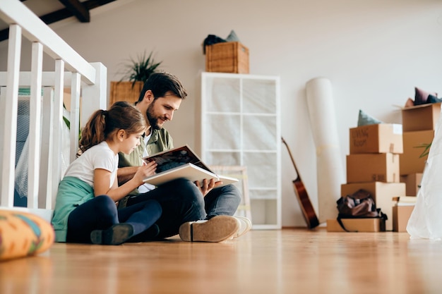 Feliz padre e hija mirando el álbum de fotos familiar en su nuevo apartamento