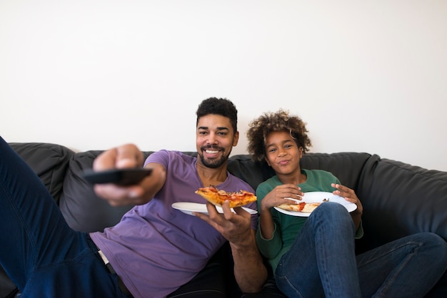 Feliz padre e hija viendo el programa de televisión favorito y disfrutando de una rebanada de pizza