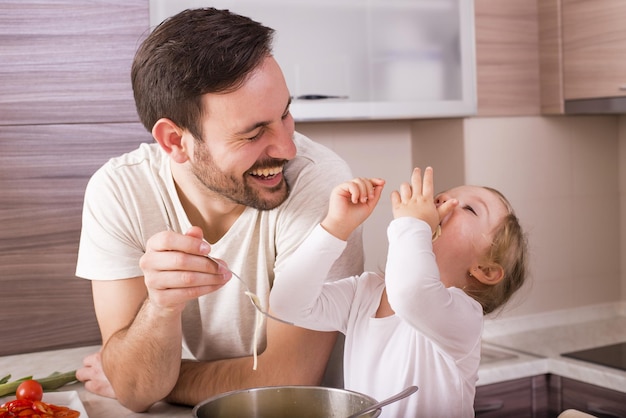 Feliz padre y su pequeña hija comiendo espaguetis caseros en la cocina